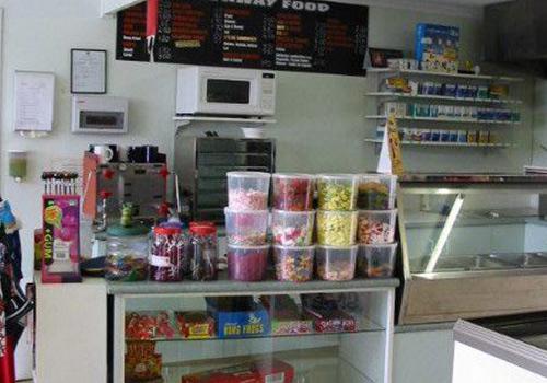 A well-stocked convenience store with shelves filled with snacks, drinks, and confectionery items, featuring a microwave and display cases for food